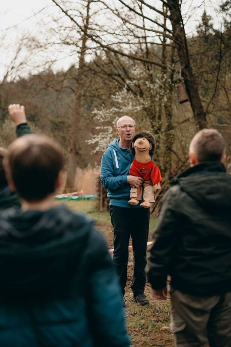 Ein Mann steht mit einer Handpuppe vor einer Gruppe Kinder